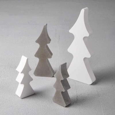 Quatro esculturas em forma de árvore de Natal, duas brancas e duas cinzentas, sobre chão cinzento.