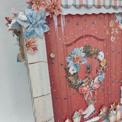 Caixa decorada com uma porta vermelha natalícia e uma coroa de flores azul e vermelha.