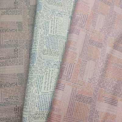 Tecidos com padrão de texto tipo recortes de jornal nas cores creme, azul claro e rosa.