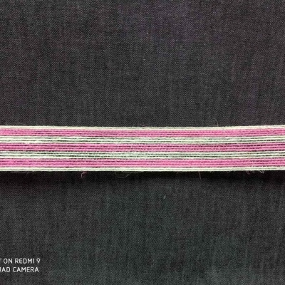 Fita decorativa riscada em rosa, branco, cinza e verde sobre tecido cinza escuro