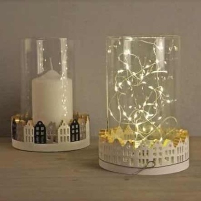 Dois castiçais decorativos com casas recortadas na base, um com vela branca e outro com luzes LED dentro de copos transparentes.