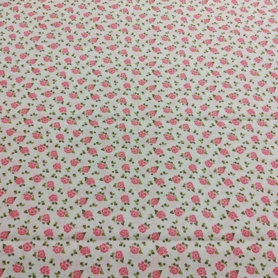 Tecido branco com padrão repetido de pequenas flores cor-de-rosa e folhas verdes