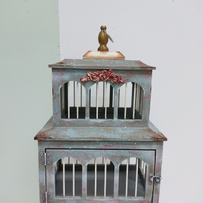 Gaiola decorativa verde com detalhes vermelhos, barras brancas e pássaro dourado no topo