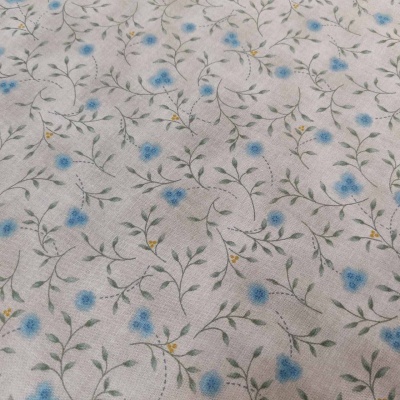 Tecido bege claro com padrão de flores azuis e folhas verdes e amarelas
