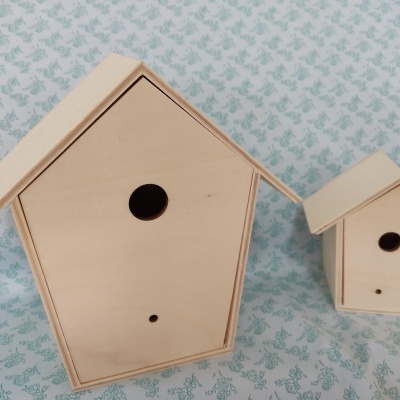 Dois ninhos de pássaros de madeira clara, um grande e um pequeno, com aberturas redondas, sobre fundo com padrão azul e branco.