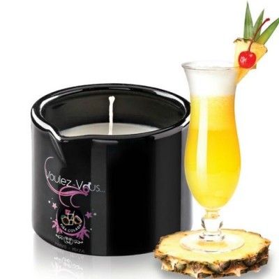 Vela perfumada em recipiente preto ao lado de cocktail amarelo decorado com ananás e cereja