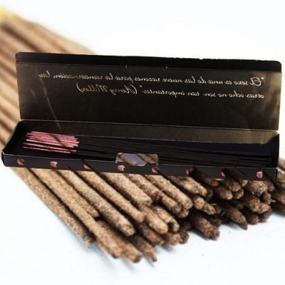 Caixa preta aberta com varetas de incenso com ponta rosa sobre fundo rústico de varetas marrons