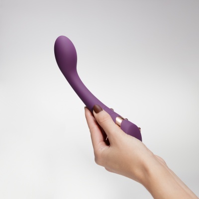 Vibrador de silicone roxo segurado por uma mão com unhas pintadas