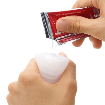 Mãos a despejar líquido de pacote vermelho para copo menstrual branco de silicone