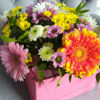 Arranjo de flores coloridas em caixa rosa sobre superfície cinzenta
