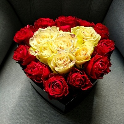 Arranjo de rosas vermelhas e amarelas em caixa preta em forma de coração numa cadeira cinza
