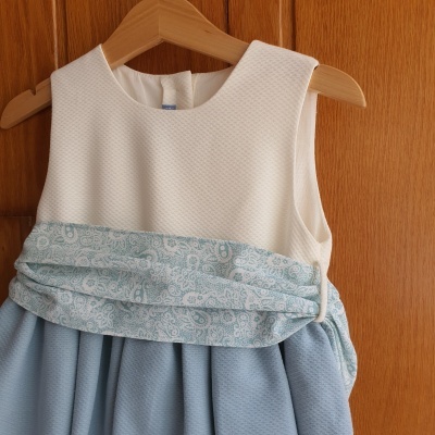 Vestido de criança azul e branco pendurado num cabide de madeira