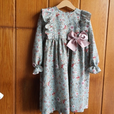 Vestido infantil azul com padrão floral e laço rosa pendurado em cabide de madeira
