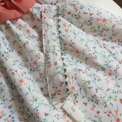 Tecido branco com padrão floral laranja e rosa, clipe branco e botão