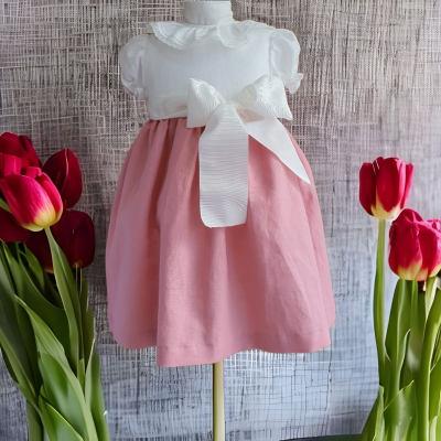 Vestido infantil branco e rosa com laço largo, em manequim, com flores vermelhas ao redor