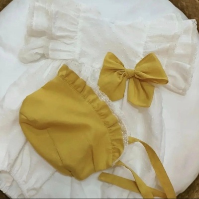 Conjunto de roupa de bebé branco com laço amarelo-mostarda e touca amarelo-mostarda com renda