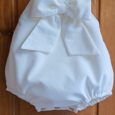 Pelele branca para bebé com laço grande pendurada num cabide de madeira