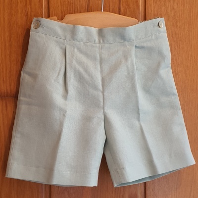 Calções cinza claro com pregas frontais pendurados numa cabide de madeira