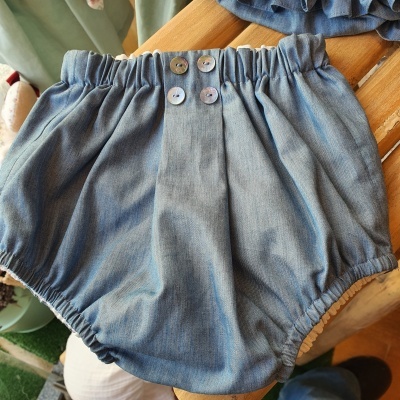 Cueca ou calção de bebê azul claro com botões decorativos em superfície de madeira