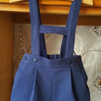 Calções azuis escuros com alças em tecido texturizado pendurados num cabide de madeira