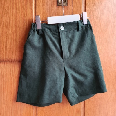 Calções verdes com botão pendurados num cabide branco contra fundo de madeira