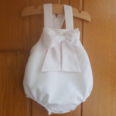 Body de bebé branco com laço e alças largas pendurado em cabide de madeira