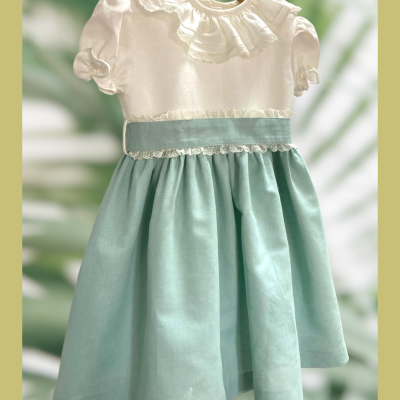 Vestido infantil branco com saia azul clara e detalhes em renda pendurado num cabide de madeira