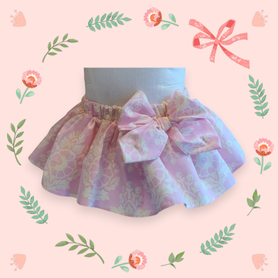 Saia infantil rosa clara com padrão floral branco e laço grande