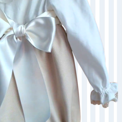 Vestido bege com laço de cetim branco e manga comprida com renda.