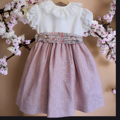 Vestido infantil branco com saia rosa e cinto floral num cabide de madeira