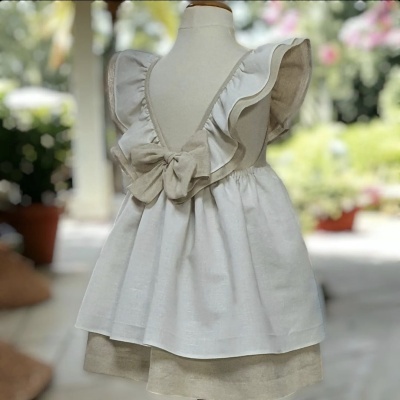 Vestido infantil branco com folhos e laço, camada inferior bege, exposto em manequim