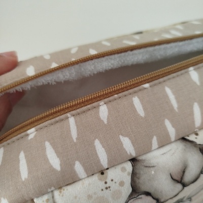 Estojo de tecido bege com penas brancas e fecho castanho aberto.