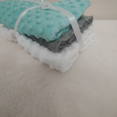 Três mantas dobradas de cores azul, cinzento e branco com textura em relevo a bolinhas.