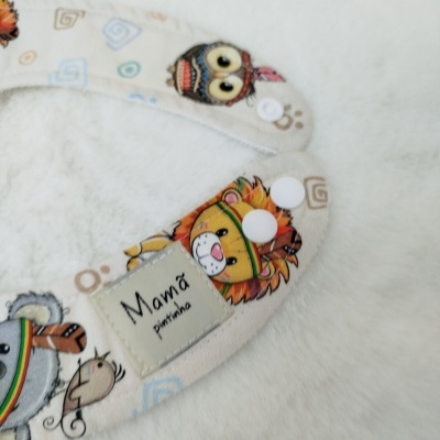 Tiras de tecido estampadas com botões brancos e etiqueta 'Mamã pintinha' sobre fundo branco felpudo