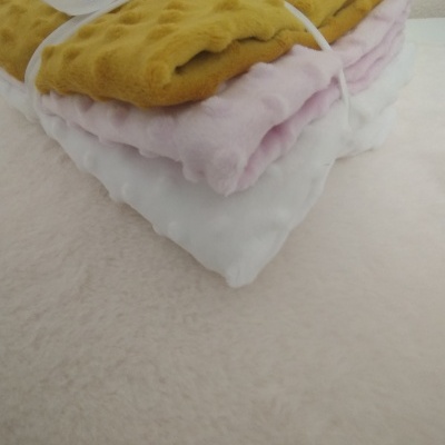 Três mantas felpudas empilhadas em amarelo, rosa claro e branco com textura de bolinhas
