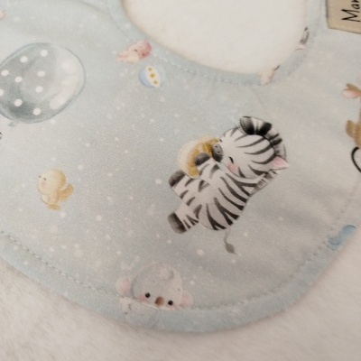 Babete azul claro com padrão de animais e detalhe branco felpudo