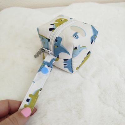 Estojo quadrado em tecido com padrão de dinossauros, fecho branco e alça azul