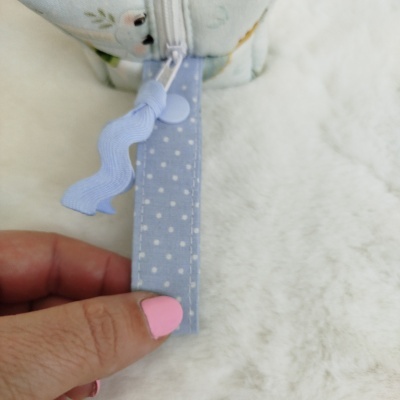 Bolsa ou estojo com zíper azul com bolinhas, mão com unhas rosa e fundo branco macio.