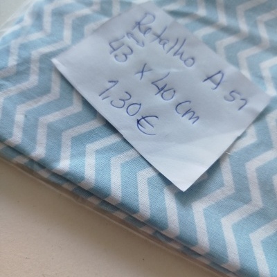 Retalho de tecido azul claro com padrão branco em zigue-zague e etiqueta com texto manuscrito.