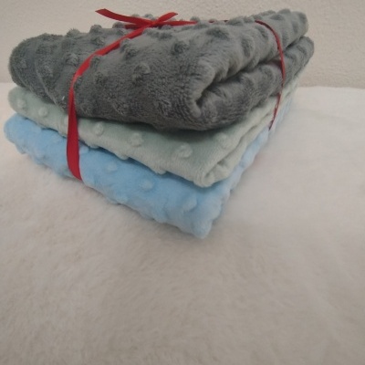 Três mantas felpudas em cinza, verde claro e azul empilhadas e amarradas com fita vermelha