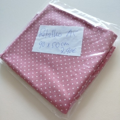 Retalho de tecido rosa com bolinhas brancas embalado em plástico com etiqueta manuscrita.