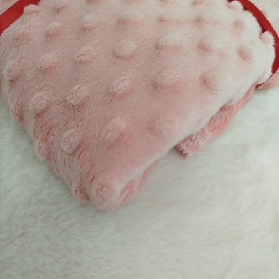 Saco de água quente com capa rosa texturizada e alça vermelha sobre tecido branco macio