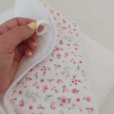 Toalha branca com padrão floral e laço segurada por mão com unhas amarelas