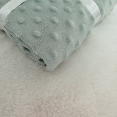 Manta cinza felpuda com bolinhas, amarrada com fita branca, sobre tecido branco felpudo