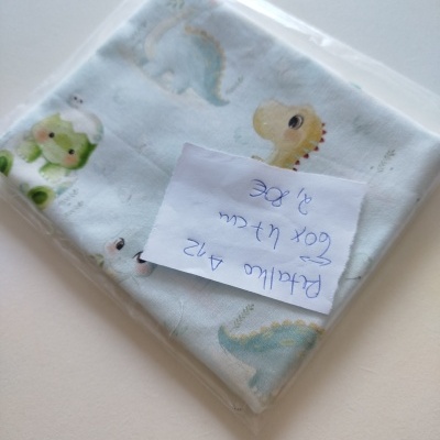 Manta azul claro com dinossauros coloridos embalada em saco plástico transparente.