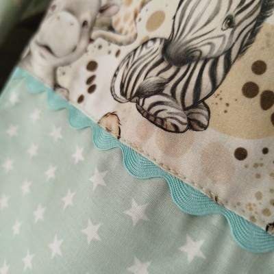 Pano infantil com estrelas brancas sobre fundo verde água, estampa de zebra e fita azul ondulada