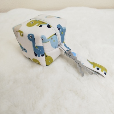 Cubo macio branco com padrão de dinossauros e fita pendurada