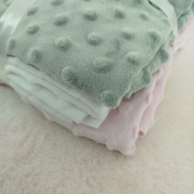 Três mantas macias com padrão de bolhas em relevo, verde, branca e rosa empilhadas