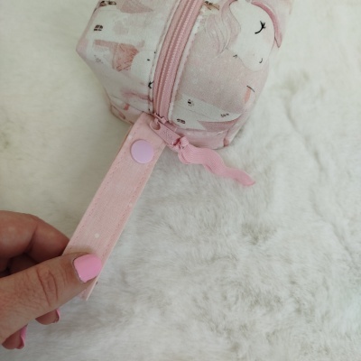 Estojo rosa com padrão de unicórnios e fecho de correr rosa sobre superfície branca felpuda