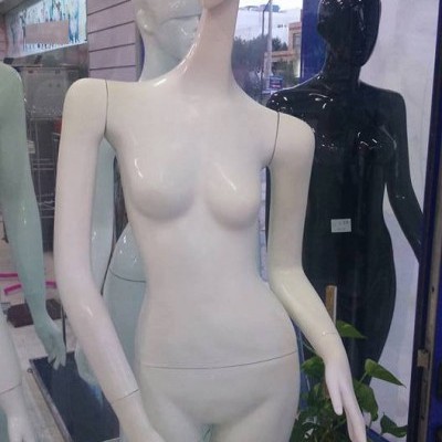 Mannequins femininos brancos, cinza claro e preto em loja com porta e planta ao fundo